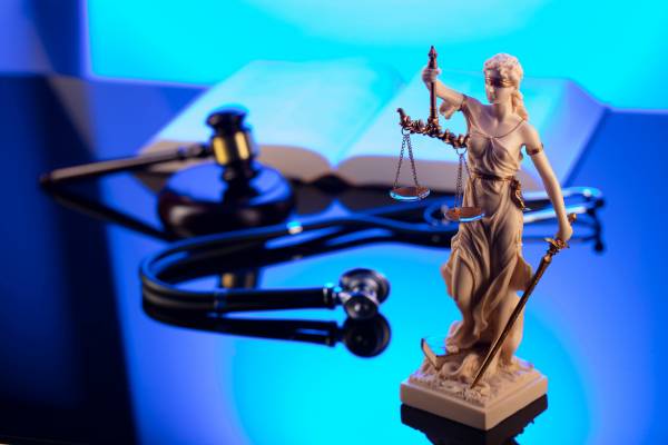 A statue of Justice, with a gavel, stethoscope, and book in the background.